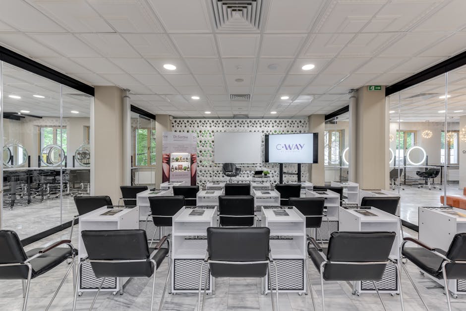 Bright and modern hair salon training area featuring rows of black chairs and equipped desks.