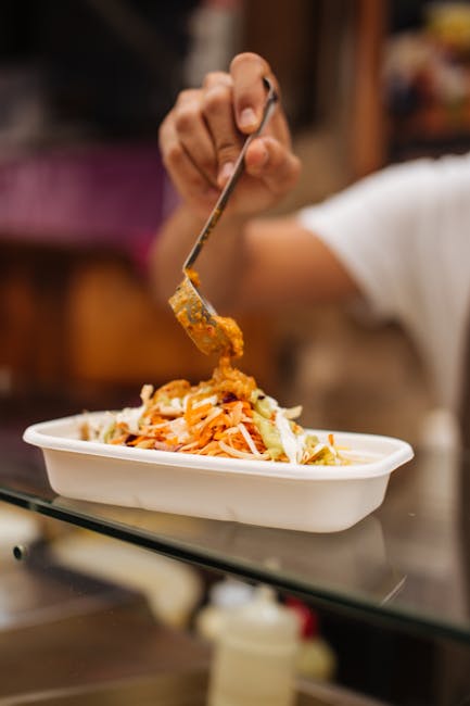 Hand serving a flavorful dish in a takeaway container, highlighting street food culture.