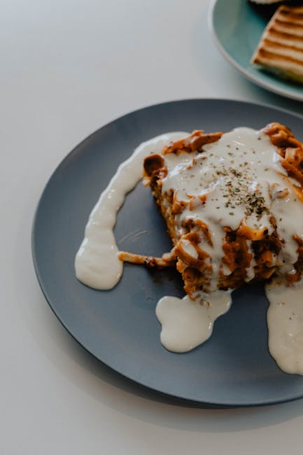 A close-up of creamy lasagna topped with white sauce on a stylish plate, perfect for food enthusiasts.