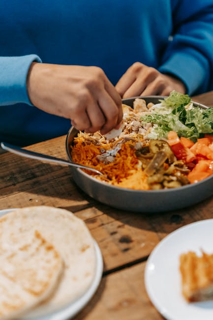 From above of crop anonymous male eating tasty dish with meat and vegetables at wooden table