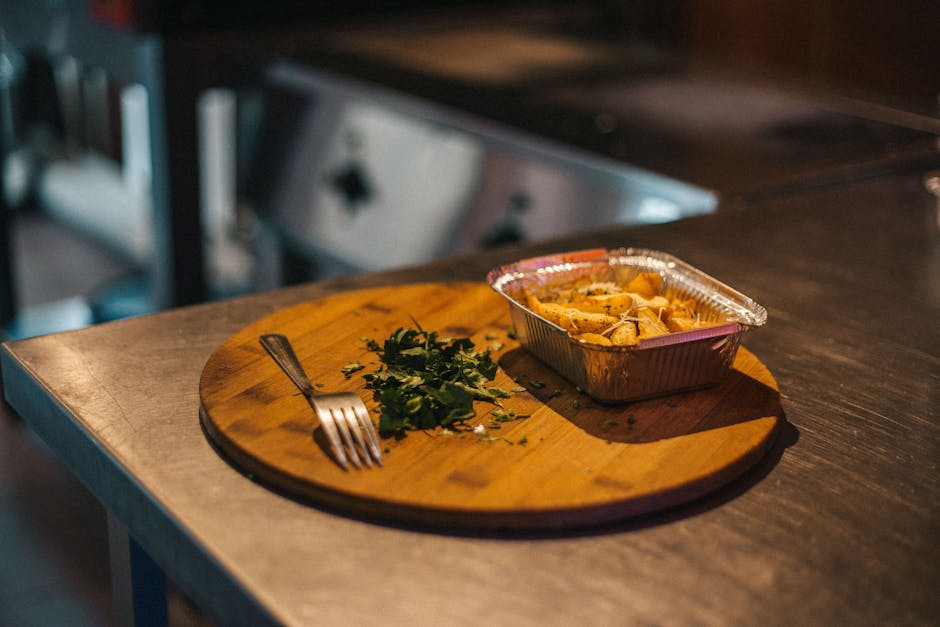 Close-up of fried potatoes in a tray on a wooden board with herbs and fork.