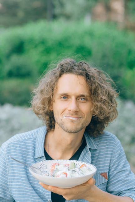 Bright image of a man with wavy hair holding a salad bowl outdoors.