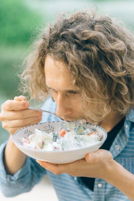 A man with curly hair savoring a fresh vegetable salad in an outdoor setting.