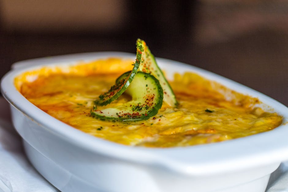 Close-up of a cheesy lasagna topped with cucumber slices, showcasing rich Italian flavors.