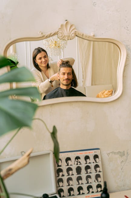 A hairdresser styles a man's hair in a well-lit salon with a mirror reflection.