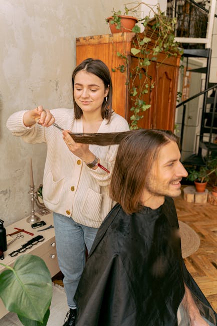 Woman stylist cutting a man's long hair in a cozy indoor salon setting.