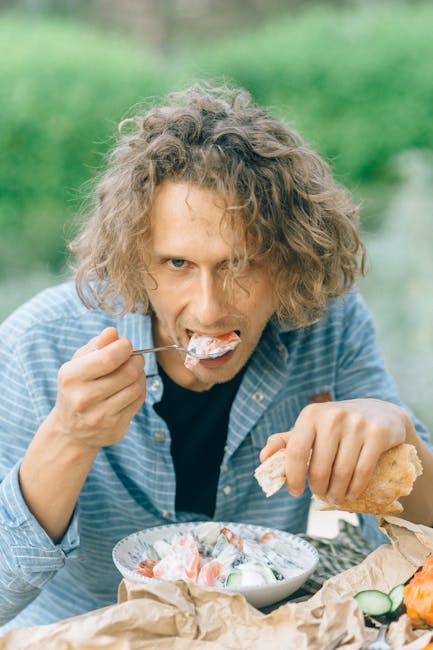 Close-up of a young man with curly hair eating a fresh vegetable salad outdoors.