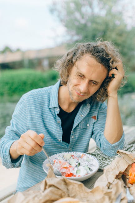 Man with curly hair eating a fresh vegan salad outdoors. Summer setting.