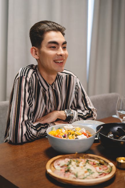 Smiling young man enjoying a dinner setting with bowls of food on a wooden table.