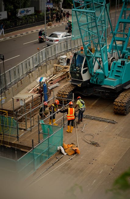 Bouwvakkers werken bij een grote blauwe kraan op een bouwplaats in de stad.