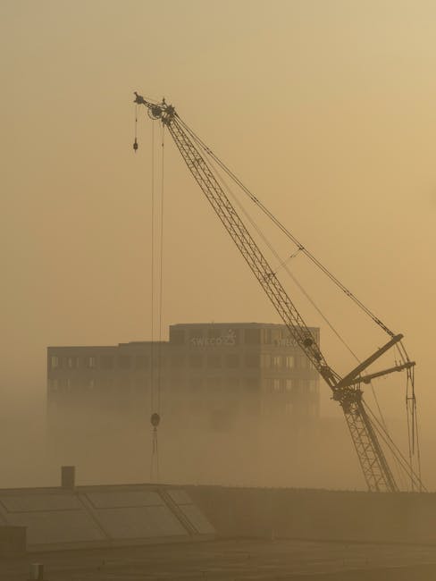 Een bouwkraan en een gebouw gehuld in de mist, mogelijk een bouwproject van Sweco.