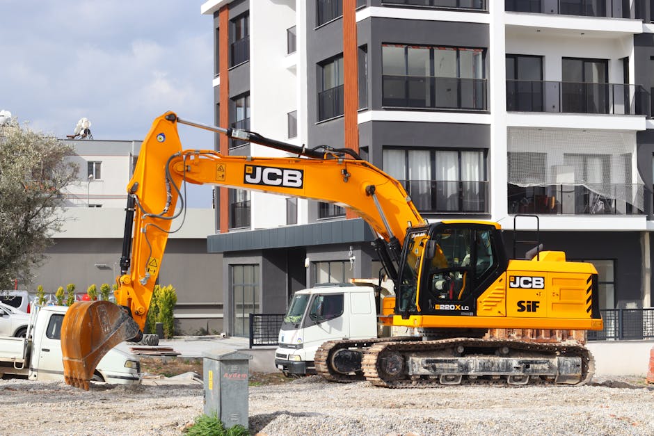 Een gele JCB graafmachine staat op een bouwplaats voor een modern gebouw.