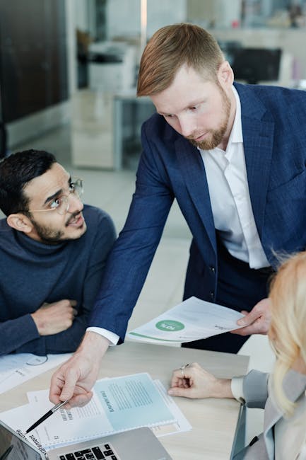 Group of colleagues engaged in a business discussion at the office, reviewing documents and using a laptop.