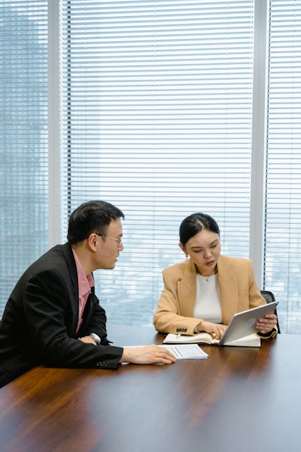 Two business professionals engaged in a meeting with a tablet in a corporate office setting.