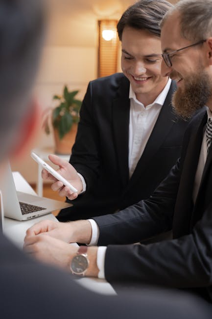 Two businessmen in black suits engaged in a friendly meeting, sharing ideas via smartphone.