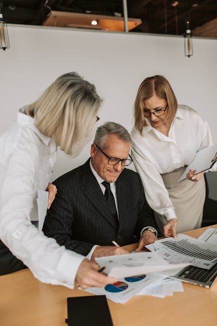 A senior businessman with colleagues discussing documents in a modern office.