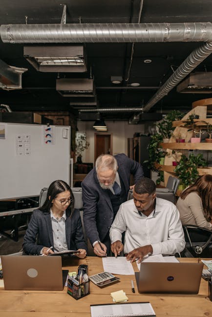 A diverse team collaborating at a table with laptops and documents in a modern office environment.