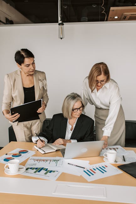 Three professional women working together on a business project with charts and laptops in a modern office.