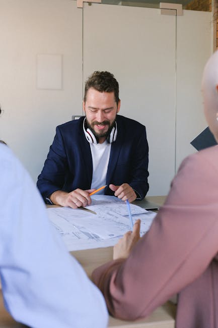 Cheerful male with crop anonymous colleagues discussing data in papers at table in conference in business office