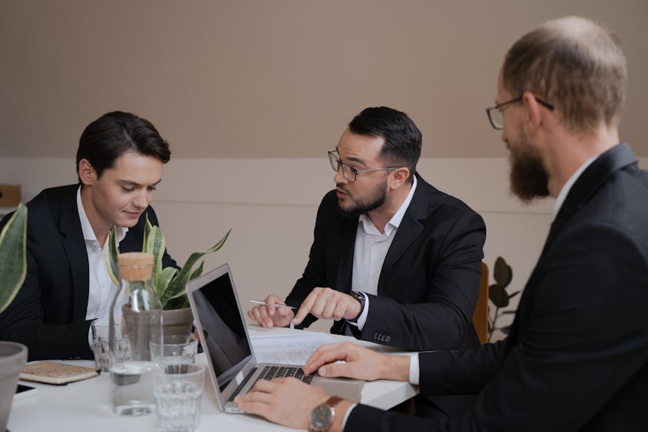 A group of businessmen engaged in a meeting, analyzing reports and using a laptop for their discussion.