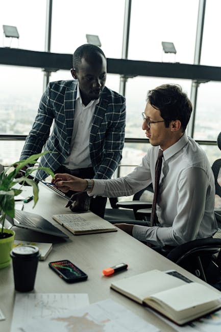 Two businessmen discussing projects in a modern high-rise office setting.