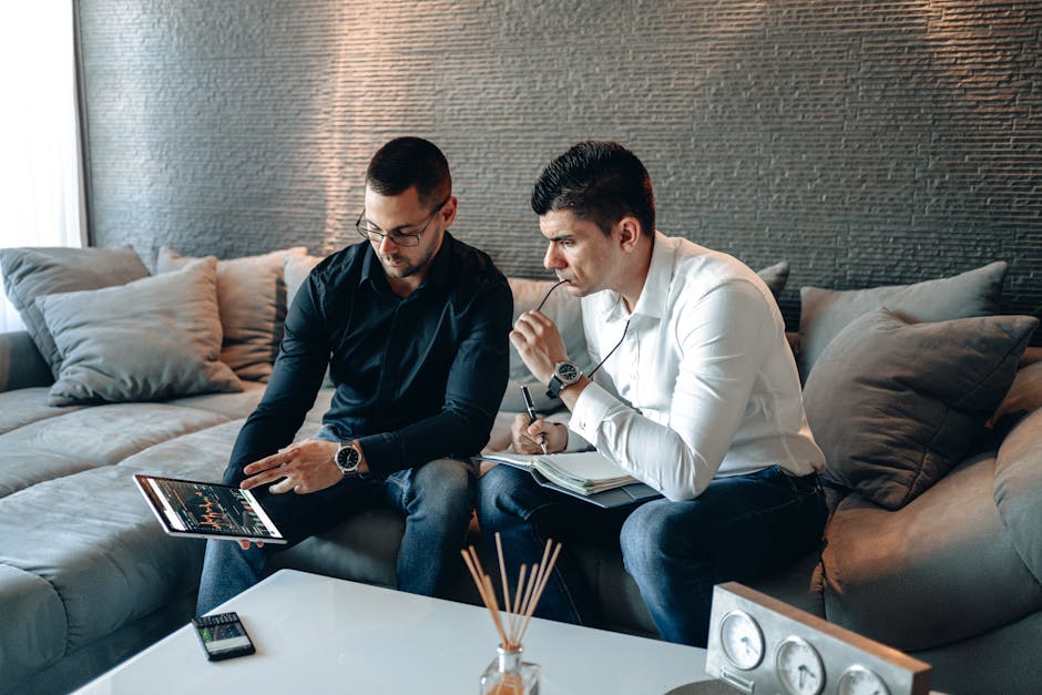 Two business professionals on a sofa analyzing financial graphs on a digital tablet indoors.