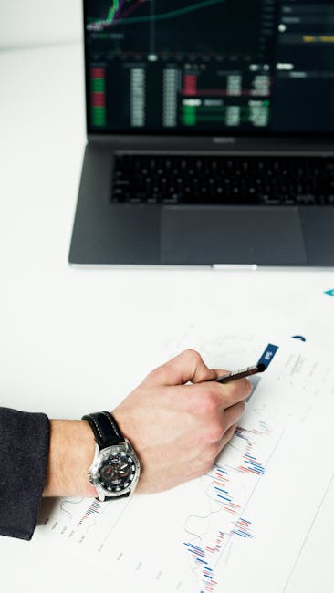 Businessperson analyzing financial charts with laptop and graphs on paper, representing stock market trends.