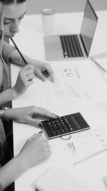 Two colleagues reviewing financial reports with a calculator in a modern workspace.