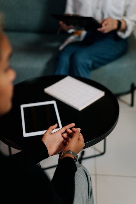 Two professionals discussing work in an office. Tablets and a notebook on the table.