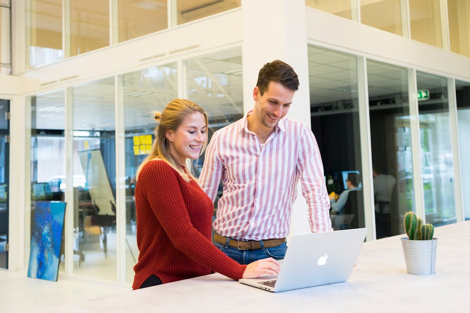 Two colleagues engaged in a positive discussion at a laptop in a modern office setting.