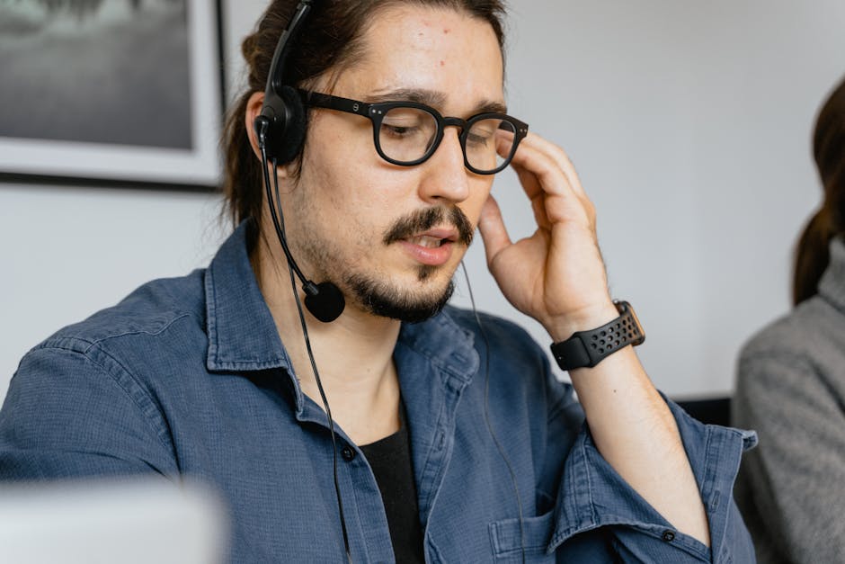 A bearded man with glasses and headphones working in a call center, providing customer support.