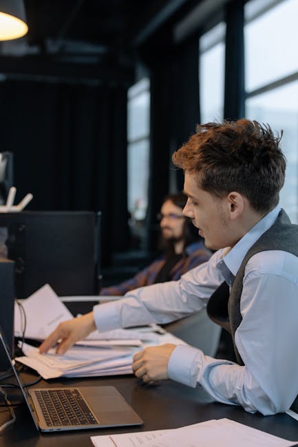 Adult male working in modern office, reviewing documents on his desk with focus and professionalism.