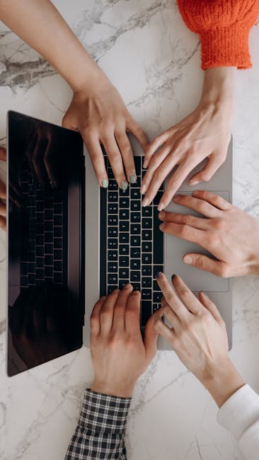 A top-down view of multiple hands typing on a laptop keyboard on a marble desk, indicating teamwork.