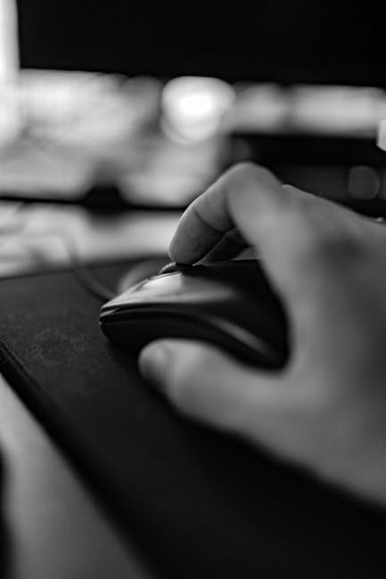 Black and white of crop anonymous worker moving mouse wheel on pad while sitting near computer on blurred background in room