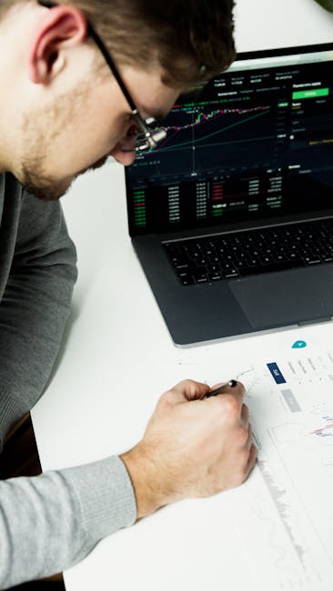 Businessman analyzing financial graphs on laptop and paper at desk.