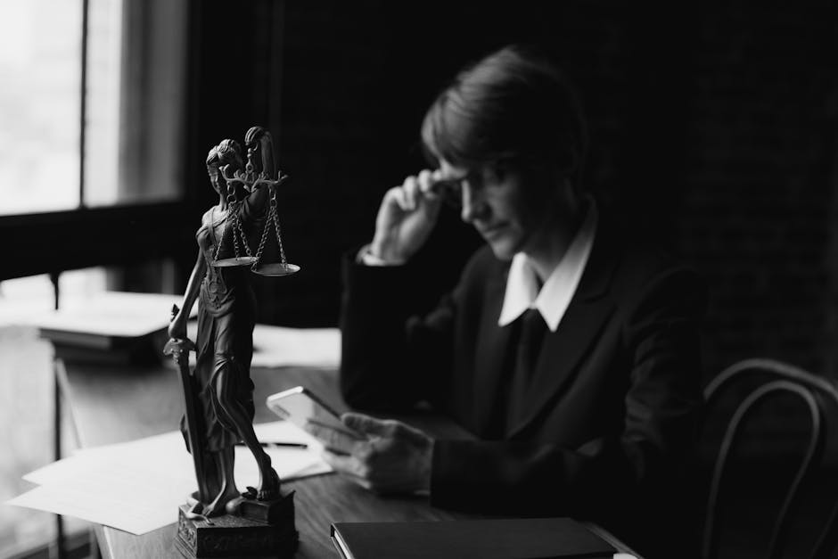 Black-and-white image of an attorney in an office with Lady Justice statue and smartphone, symbolizing modern legal concepts.