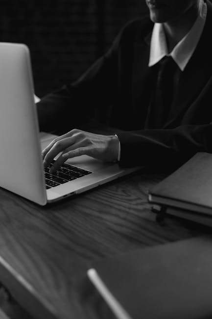 A business professional wearing a suit types on a laptop, captured in a grayscale artistic style.