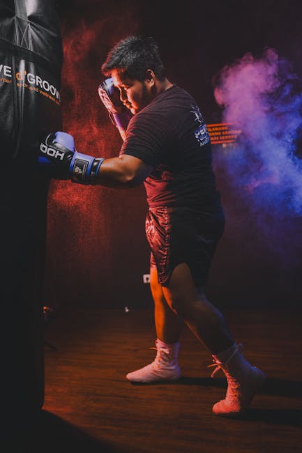 A boxer intensely trains with a punching bag in a dimly lit gym.