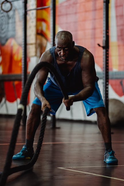 A muscular man engages in a powerful battle rope workout inside a gym, focusing on strength and endurance.