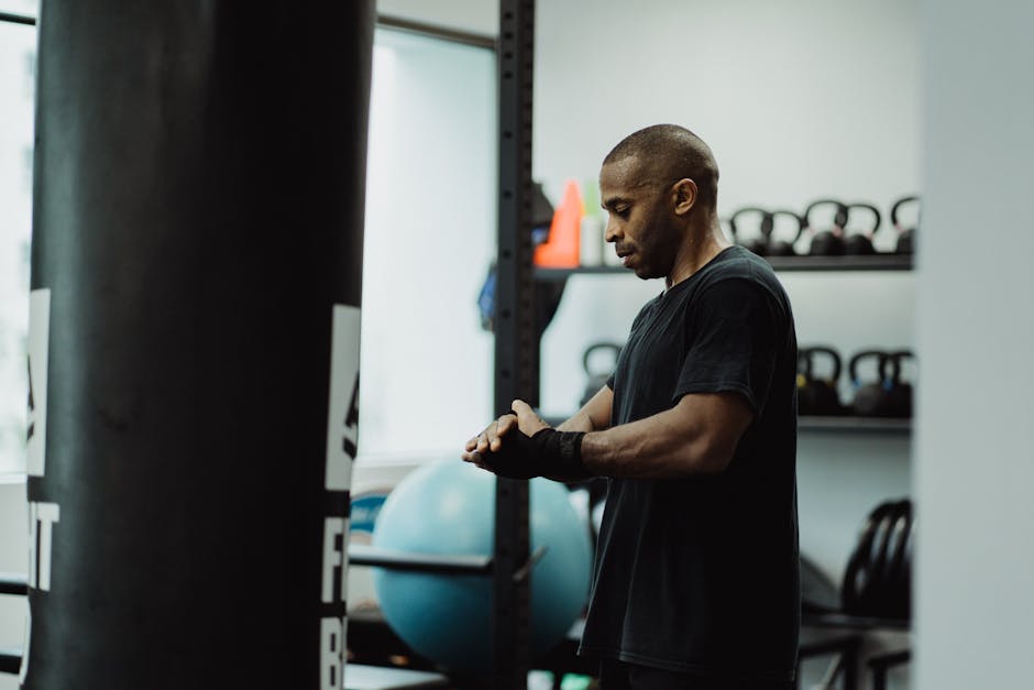 A man in a gym prepares for a workout, wrapping his hands next to gym equipment.