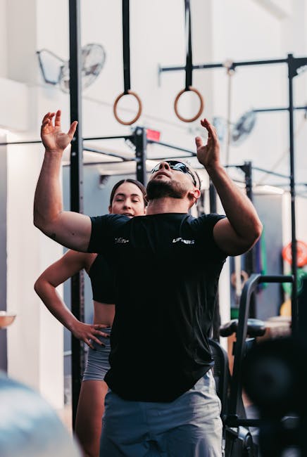 Athletic man and woman exercising with gymnastic rings indoors in a modern gym setting.