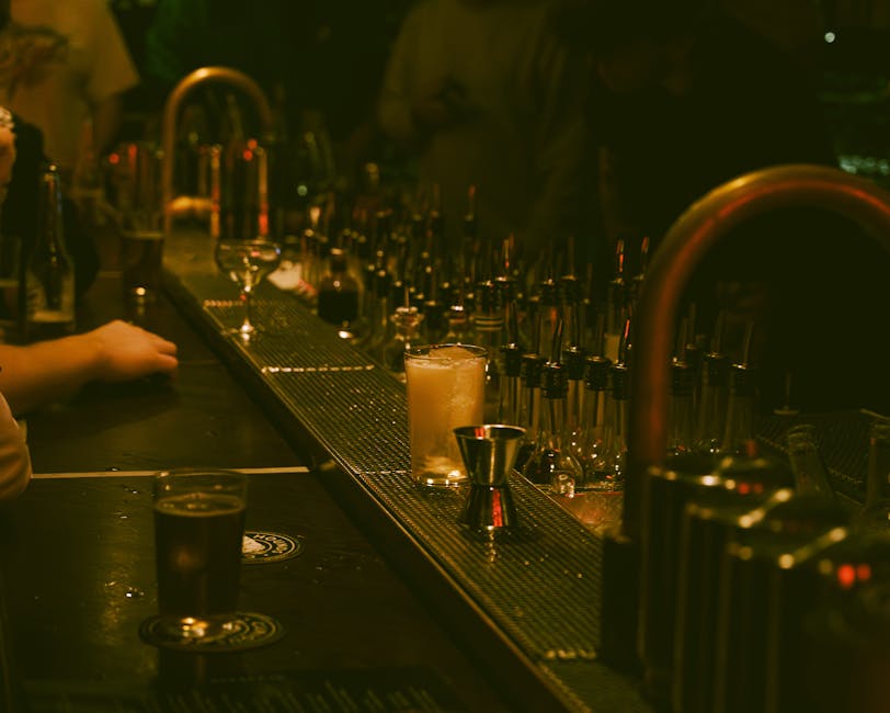 A dimly lit bar with a drink and bar tools creating a moody atmosphere.