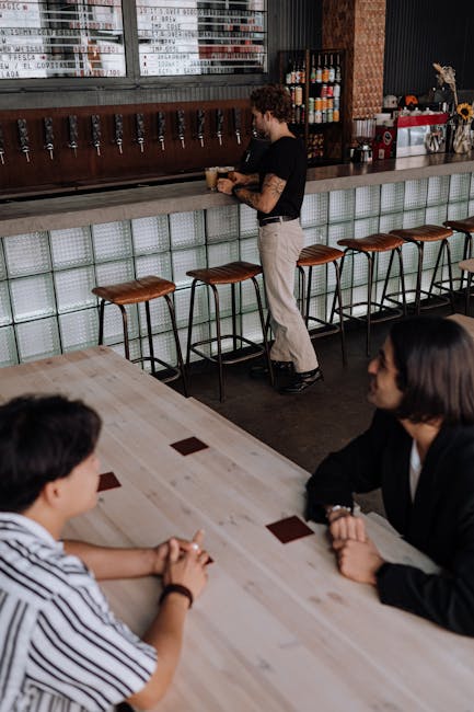 A modern brewpub interior with friends chatting at a table while bartender prepares drinks.