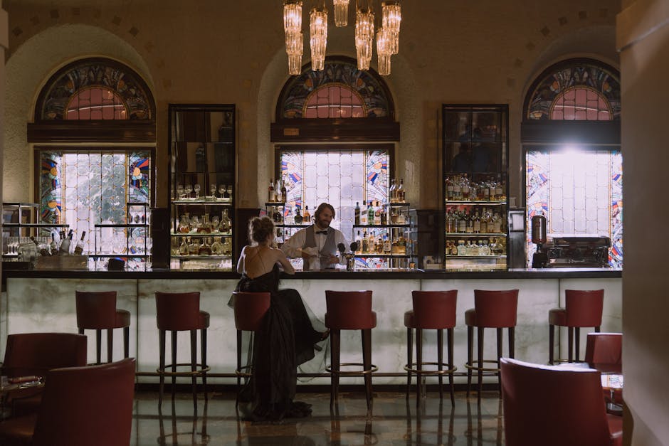 A woman in a black dress enjoys a conversation with a bartender in a stylish, luxurious bar.