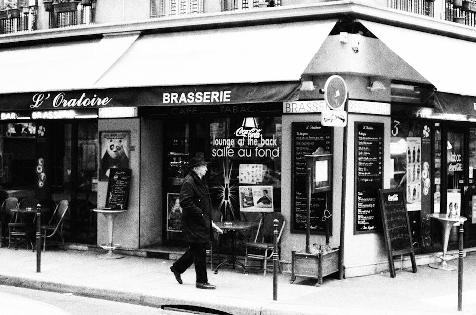 Black and white photo of a Parisian brasserie with a person walking by, capturing a classic street scene.