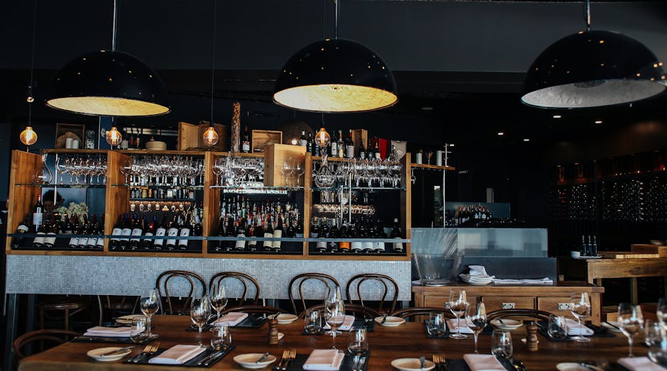 Stylish bar interior featuring pendant lamps, wooden furnishings, and a well-stocked bar area.