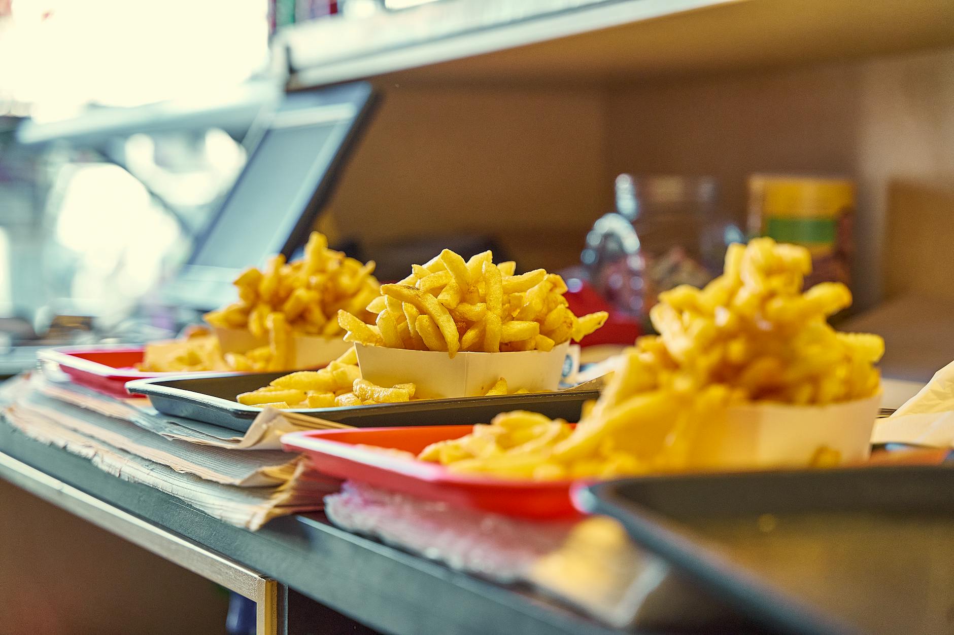 Verse frietjes in kartonnen bakjes op een toonbank, klaar om geserveerd te worden.