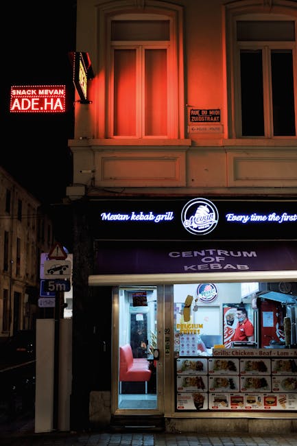 Night view of a vibrant kebab shop in Brussels with glowing signboards and street lamp.