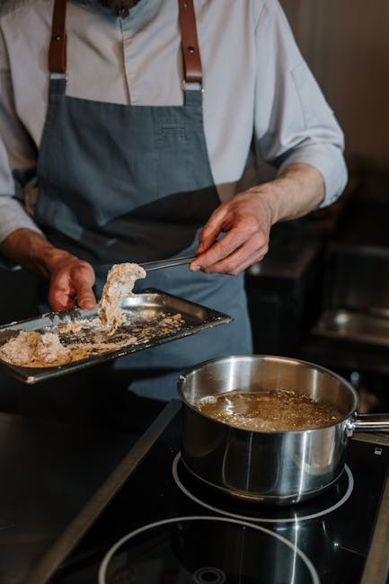 A chef skillfully coating food in breadcrumbs beside a saucepan in a professional kitchen.