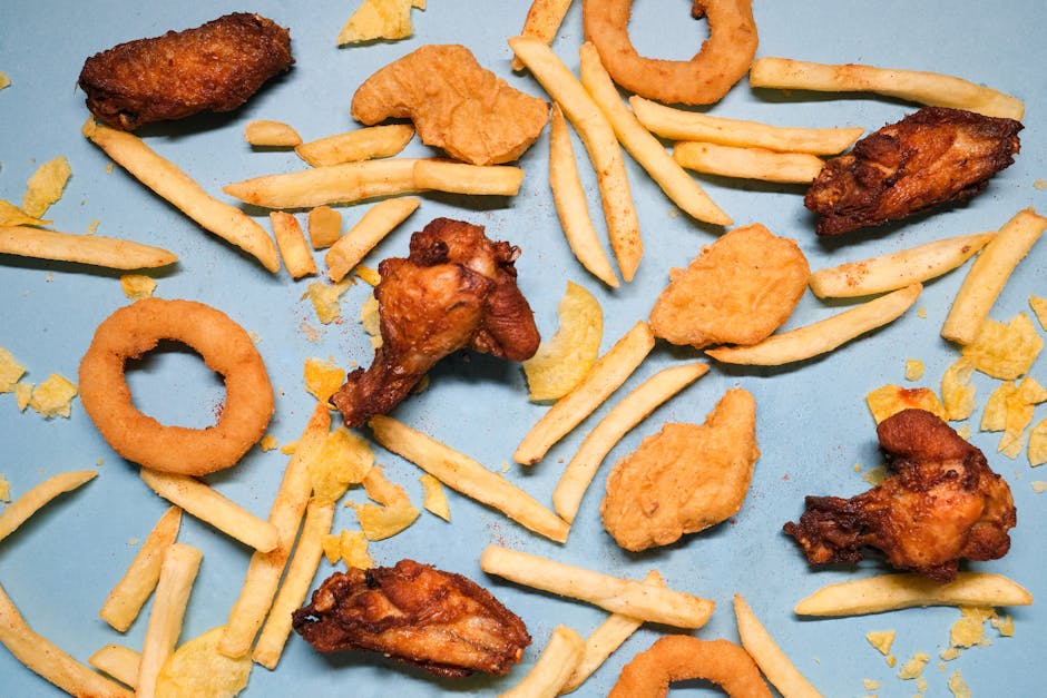 Flat lay of assorted fried snacks including chicken wings, french fries, and onion rings on a blue surface.